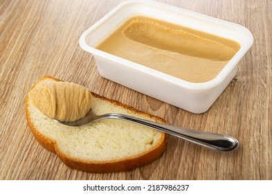 Teaspoon With Peanut Butter On Slice Of Bread, Plastic Box With Sweet Peanut Paste On Wooden Table