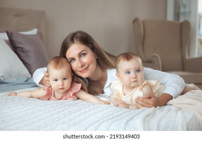 Tebder Portrait Of Smiling Happy Mother Lying On Bed With Two Little Twin Daughters 6 Month Old At Comfortable Home With Pastel Colors Interior