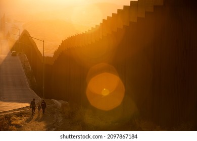 Tecate, Baja California, Mexico - September 14, 2021: Late Afternoon Sun Shines On The USA Mexico Border Wall People Walk In Front Of It.