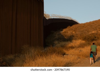 Tecate, Baja California, Mexico - September 14, 2021: Late Afternoon Sun Shines On The USA Mexico Border Wall People Walk In Front Of It.