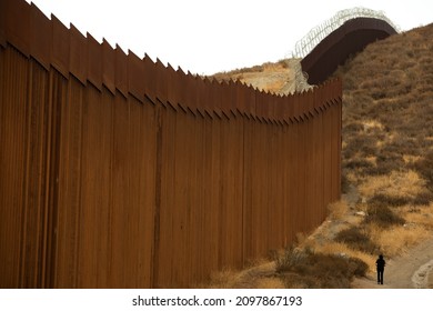 Tecate, Baja California, Mexico - September 14, 2021: Late Afternoon Sun Shines On The USA Mexico Border Wall People Walk In Front Of It.