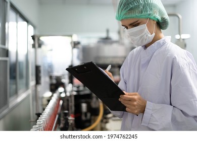 A tech expert or inspector is taking notes on the clipboard to verify orders on the food factory production line. Production control workers