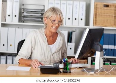 Tech Savvy Elderly Woman Working On The Computer And Smiling, Sitting Inside Her Office.