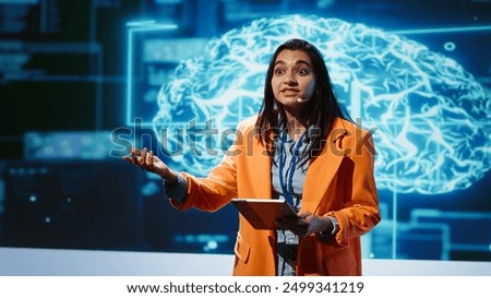 Tech startup leader using convention as platform to offer latest AI services. Businesswoman holding tablet uses microphone to talk with investors interested in artificial intelligence, camera A