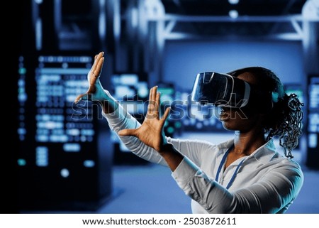 Tech support in data center uses virtual reality to prevent system overload. BIPOC VR technology user in server room ensuring enough network bandwidth for smooth operations