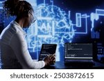 Tech support updates neural networks made of interconnected nodes, writing intricate binary code scripts on tablet and laptop. Server hub employee uses programming to upgrade AI simulation model