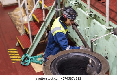 Technical crew member performing mechanical repair on marine diesel exhaust system.