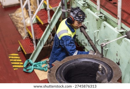 Technical crew member performing mechanical repair on marine diesel exhaust system.