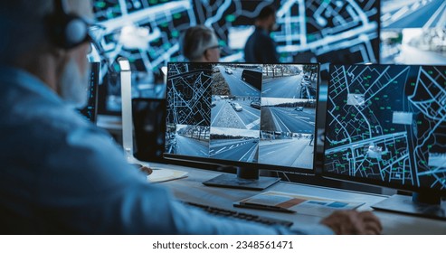 Technical Customer Support Specialist is Talking on a Headset while Working on a Computer in a Call Center Control Room Filled Display Screens with Monitoring Software. Over the Shoulder Footage