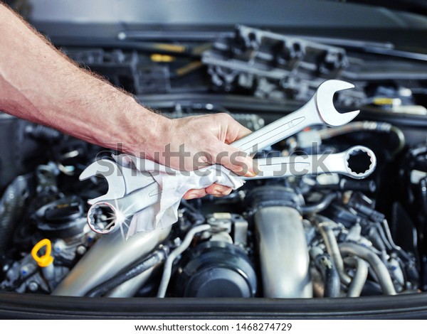 a technical employee of a car service workshop
hold some tools in front of an open bonnet and you see the motor
engine in the background