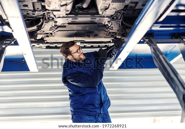 Technical inspection\
of the car. Car diagnostics on technical inspection. A man in a\
blue uniform stands in a canal in the garage and fixes a car\
problem, a foreman in a\
workshop