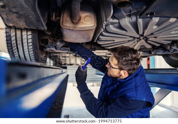 Technical inspection of the car. Car service in\
workshop. A man in a blue uniform stands under a car in a garage\
and checks the condition of the brakes on car tires.\
Troubleshooting\
motorcar
