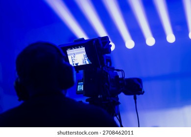 Technical livestream scene with a camera operator filming illuminated stage beams as real time video feed appears on the onboard monitor during event production