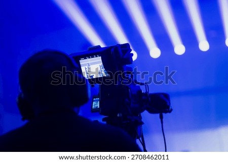 Technical livestream scene with a camera operator filming illuminated stage beams as real time video feed appears on the onboard monitor during event production