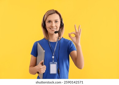 Technical support call center. Smiling operator with laptop showing ok gesture on yellow background