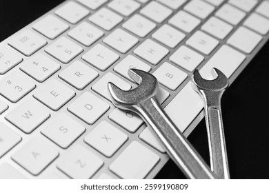 Technical support concept. Wrenches and keyboard on black background, closeup