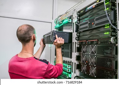 Technical Support Engineer performs the installation of a new server in a rack with computer equipment. The man is working in the server room of the data center