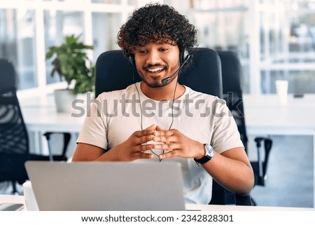 Technical support operator working with headset in office. Smiling handsome man working as call centre operator, speaking to customer. Happy businessman working remotely while doing video conference.