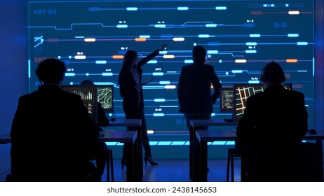 Technical support team in control room. Man and woman specialists discussing work, digital screen shows infrastructure monitoring infographic network data.