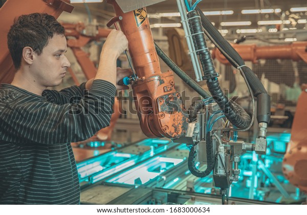 Technical worker performs maintenance robotic arms\
on the production\
line