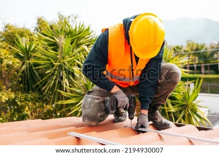 Technical worker works with drill on the roof of a house