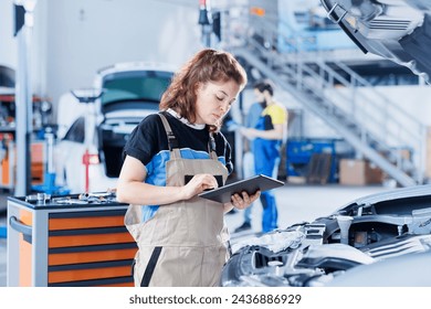 Technician in car service uses tablet to calculate invoice for client after repairing fuel tank. Competent garage employee calculating final costs after servicing customer vehicle