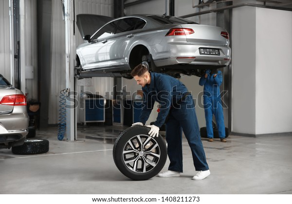 Technician with\
car wheel in automobile repair\
shop