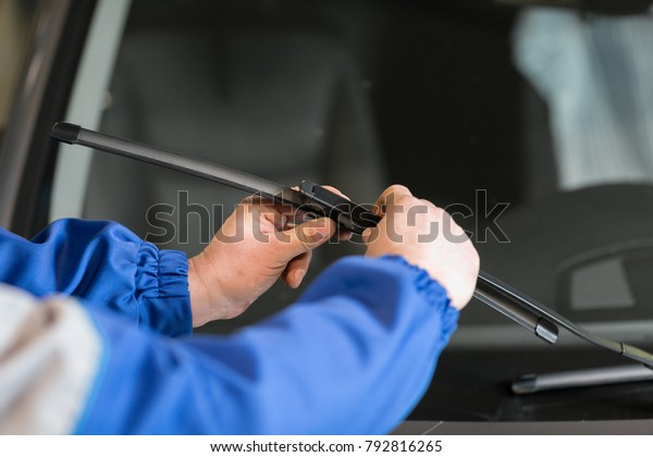 Technician is changing windscreen wipers on a\
car station.
