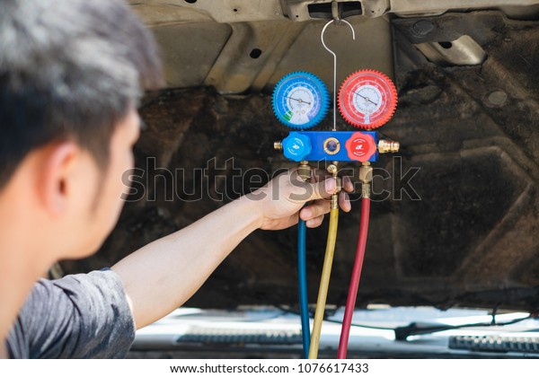 Technician check air car system. Mechanic\
repairing car using Manifolds Gauge air conditioning in auto\
vehicle fill refrigerant in car\
garage.