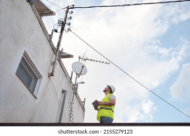 Technician Checking Electric Wire Power Lines And Telephone Pole In A House Roof Of A Residential Area.