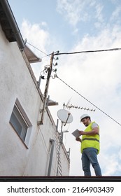 Technician Checking Electric Wire Power Lines And Telephone Pole In A House Roof Of A Residential Area.