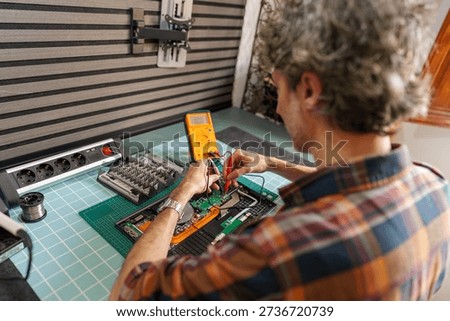 Technician checking electronic device circuit board with multimeter, diagnosing and repairing hardware problem