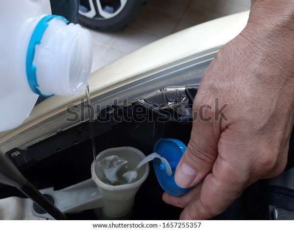 Technician is checking level of windshield\
washer fluid  at car care service Before\
Travel.
