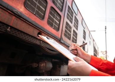 A technician is checking on heavy machine maintenance checklist, with train locomotive engine cabin part as blurred background. Transportation industrial working scene, selective focus at hand.