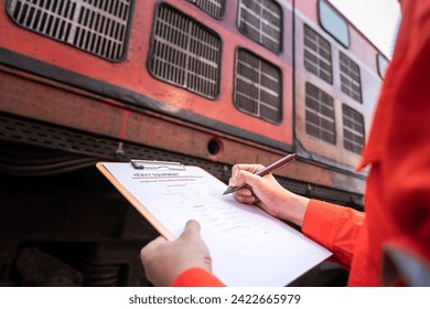 A technician is checking on heavy machine maintenance checklist, with train locomotive engine cabin part as blurred background. Transportation industrial working scene, selective focus at hand.