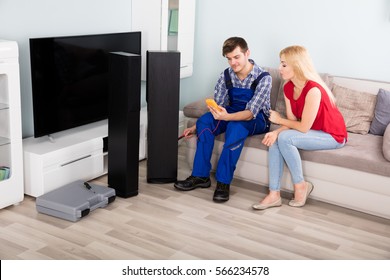 Technician Checking TV Speaker Sound System With Multimeter In Front Of Woman At Home