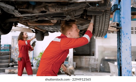 Technician checks the car maintenance data from the tablet to find out the car's faults. Caucasian man helping to fix a car that was lifted for undercarriage repairs in garage. in auto repair shop - Powered by Shutterstock