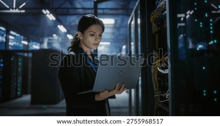 Technician checks server racks and analyzes network systems on a laptop in a data center. The facility has glowing server information technology and internet device service support.