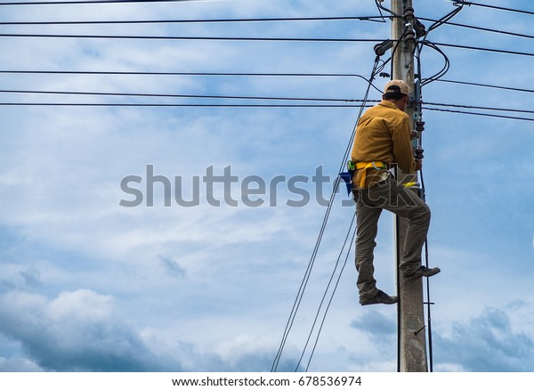 The technician is climbing on the\
electric pole for repairing electric problems in the background of\
cloudy blue sky, concept of risk for hazardous\
work.
