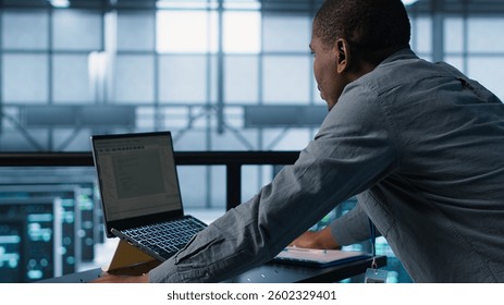 Technician coding on laptop in data center, managing server virtualization, finetuning network protocols. Server farm employee programming on notebook, enforcing advanced security measures, camera A