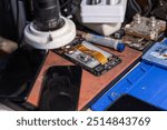 A technician conducts a battery replacement for a mobile phone on a workbench filled with various tools in a repair shop.