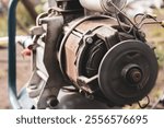 A technician conducts maintenance on a large industrial motor in an outdoor workshop. The motor is partially disassembled, revealing its inner workings and components.