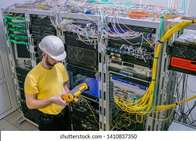 A technician diagnoses a problem area in a telecommunication network. The engineer in a white helmet measures the level of the optical signal in the server room of the data center