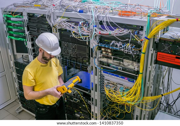 A technician\
diagnoses a problem area in a telecommunication network. The\
engineer in a white helmet measures the level of the optical signal\
in the server room of the data\
center