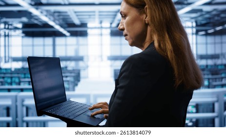 Technician doing checkup, inputting data on laptop of needed server hub fixes. Close up of employee working in data center housing advanced storage infrastructure supporting IT workloads, camera B