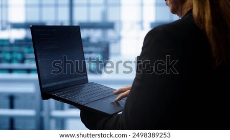 Technician doing checkup, inputting data on laptop of needed server hub fixes. Close up of employee working in data center housing advanced storage infrastructure supporting IT workloads, camera A