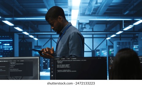 Technician doing system analysis using tablet, doing needed adjustments in supercomputers server farm. Engineer overseeing data center housing storage infrastructure supporting critical IT workloads - Powered by Shutterstock