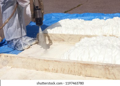 Technician dressed in a protective white uniform spraying foam insulation using Plural Component Spray Gun. Spraying polyurethane foam for roof and energy saving