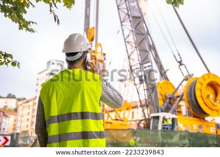Technician engineer observing the team of workers at the construction site in the city, talking on the phone