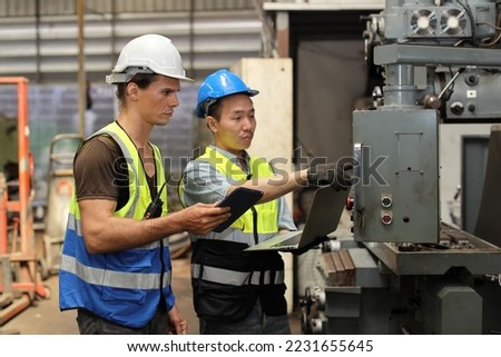 Technician engineer in protective uniform with hardhat standing and teaching apprentices or colleague worker to use computerized machine control at heavy industry manufacturing factory